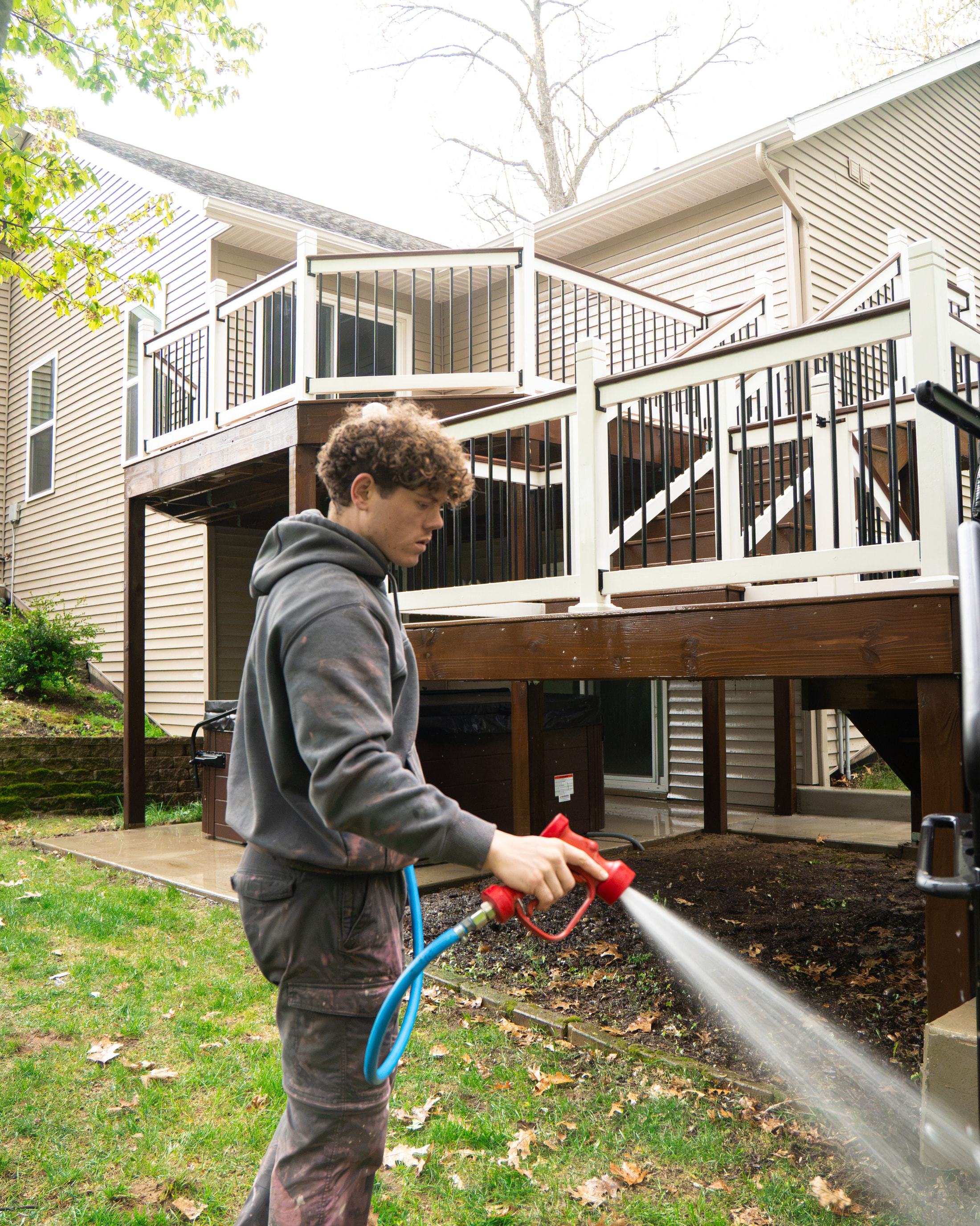 Technician washing beside a two-tier stained wood deck with white vinyl railings