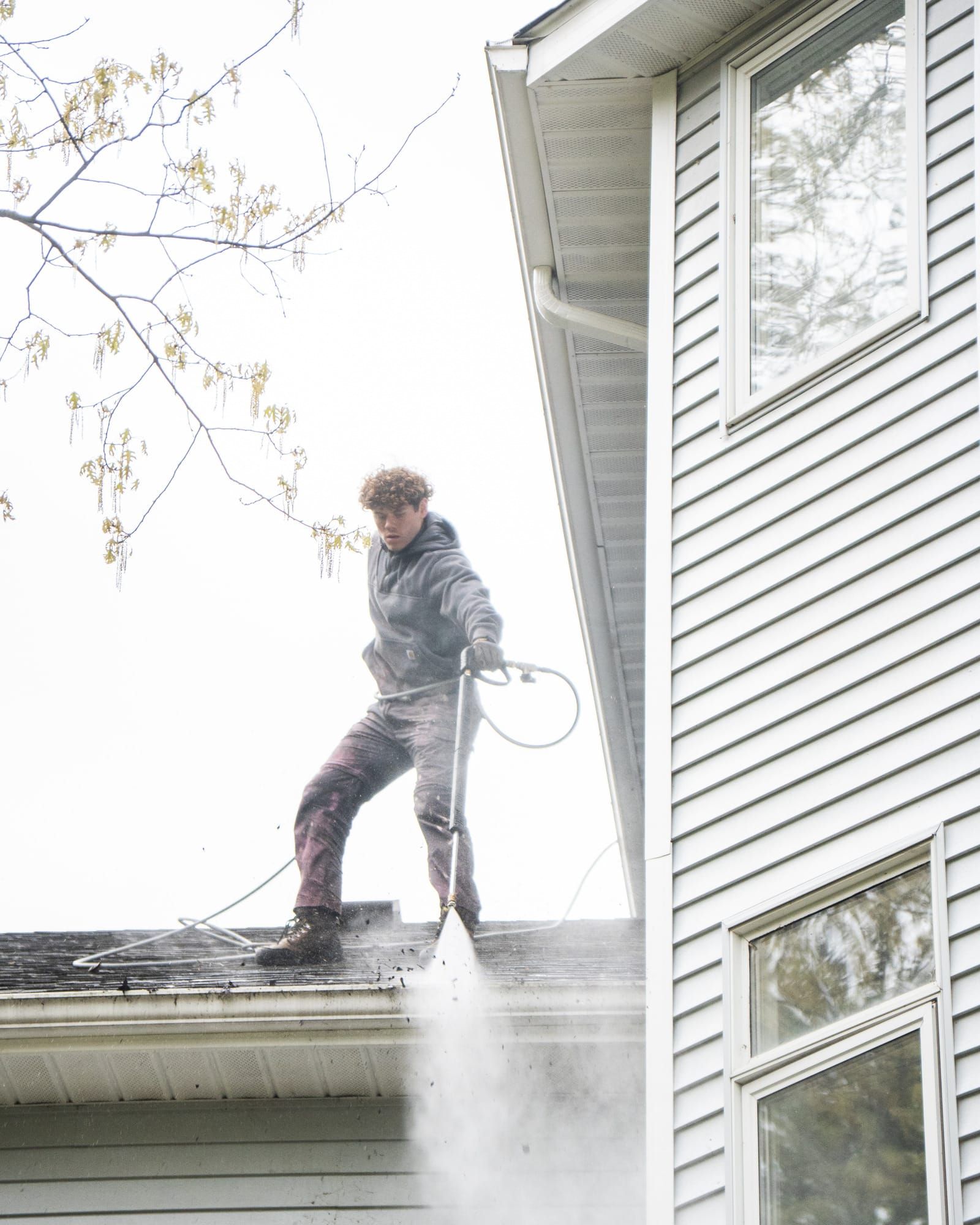 Elevation technician clearing a home's gutters from the roof, debris flushing out over the roof edge