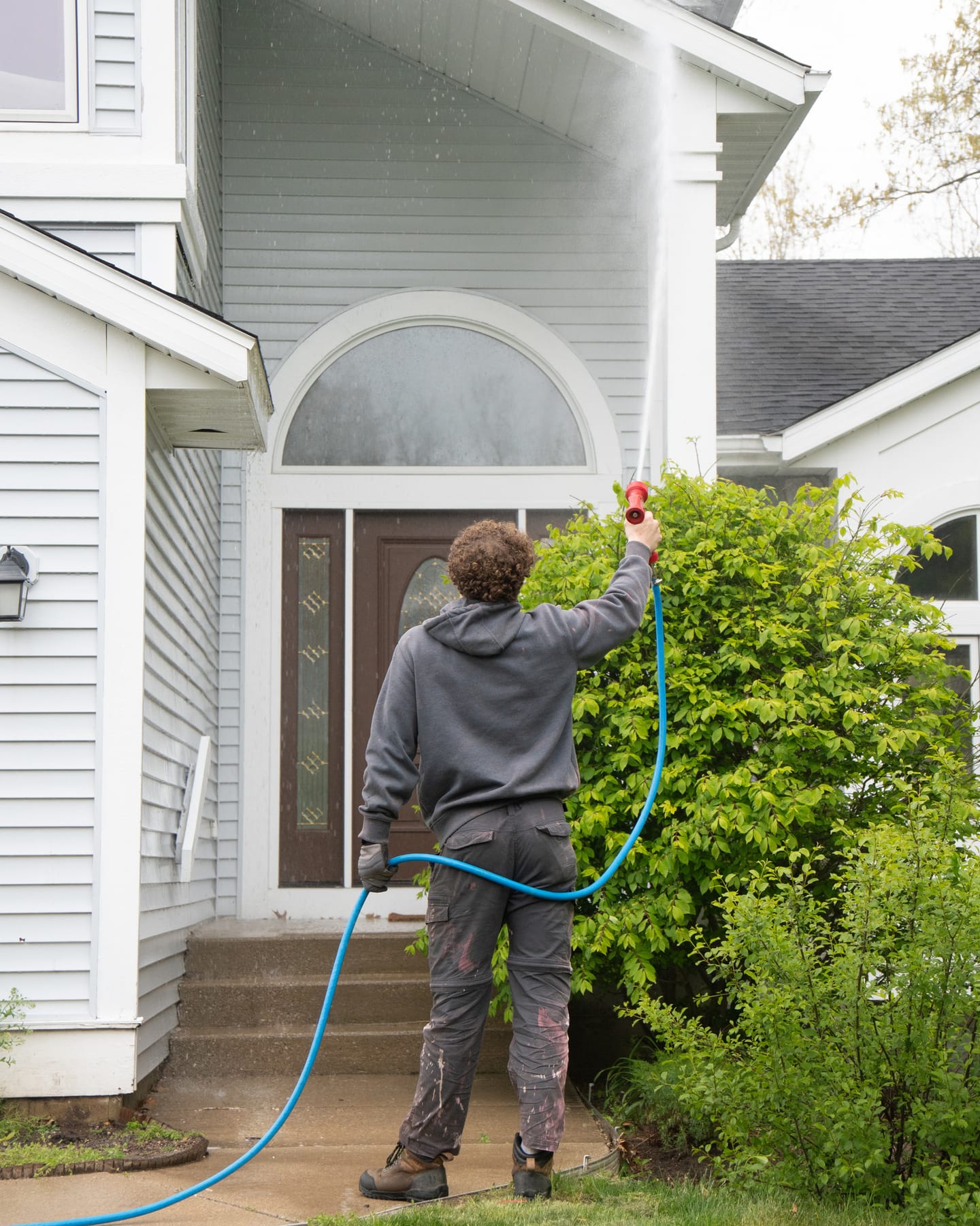 Technician soft-washing the gable and eave above a home's arched front entry