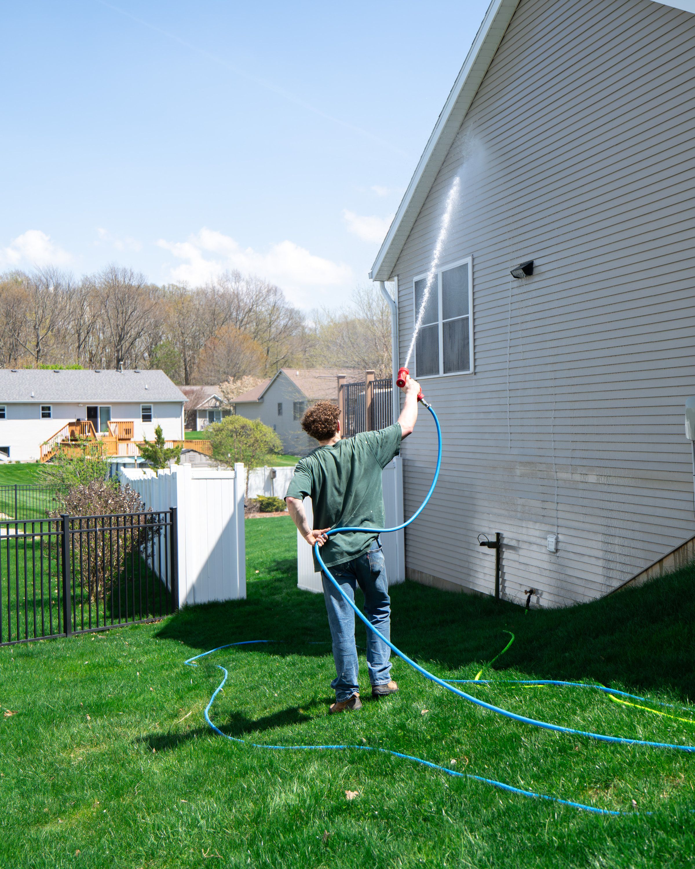 White vinyl fence line running along a back yard while an Elevation technician soft-washes the house behind it