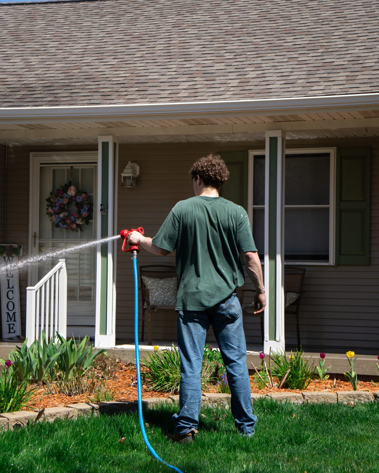 Technician soft-washing the covered front porch and siding of a single-story ranch home