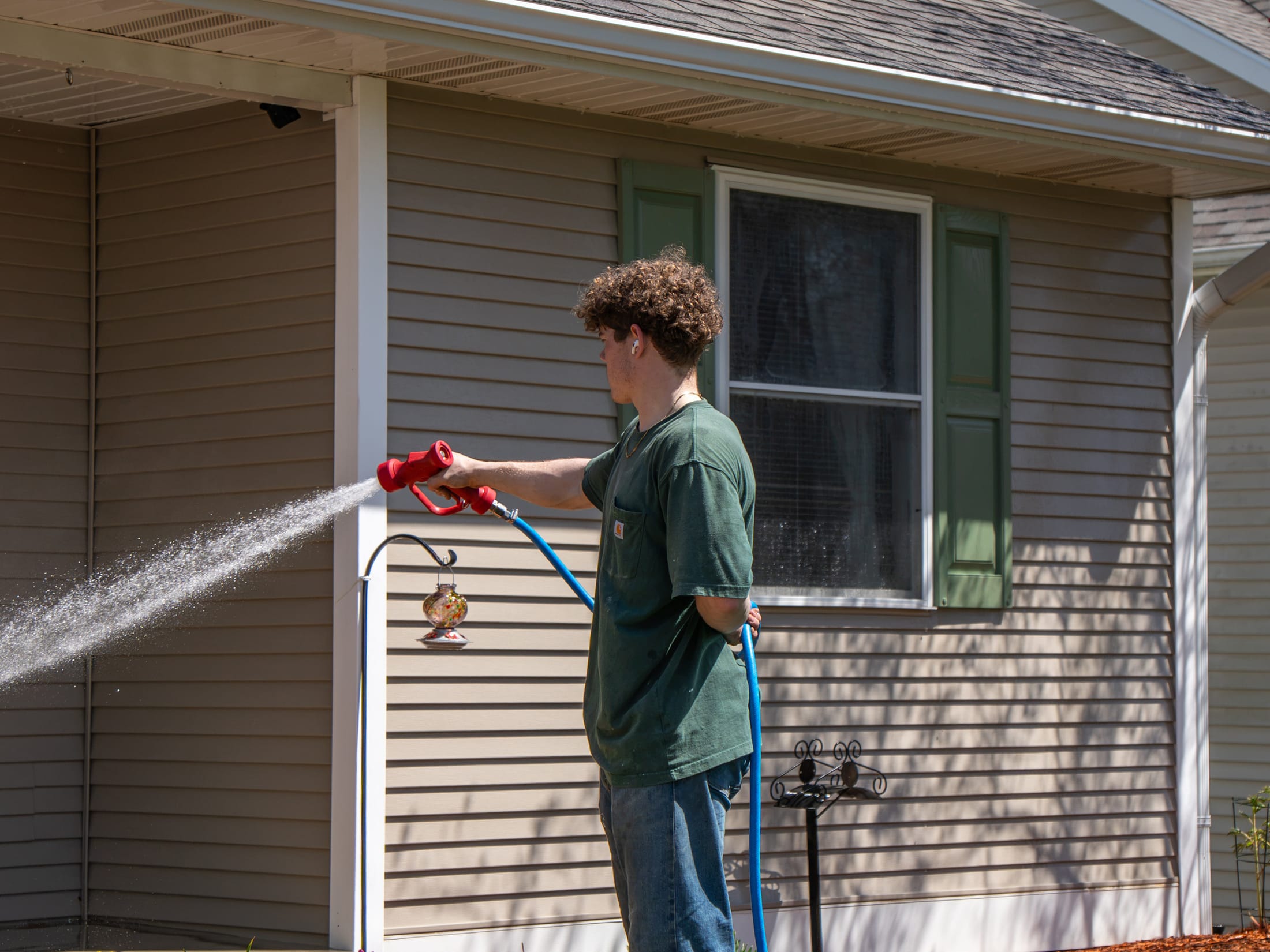 Elevation technician soft-washing vinyl siding and soffit on a single-story home with a low-pressure spray