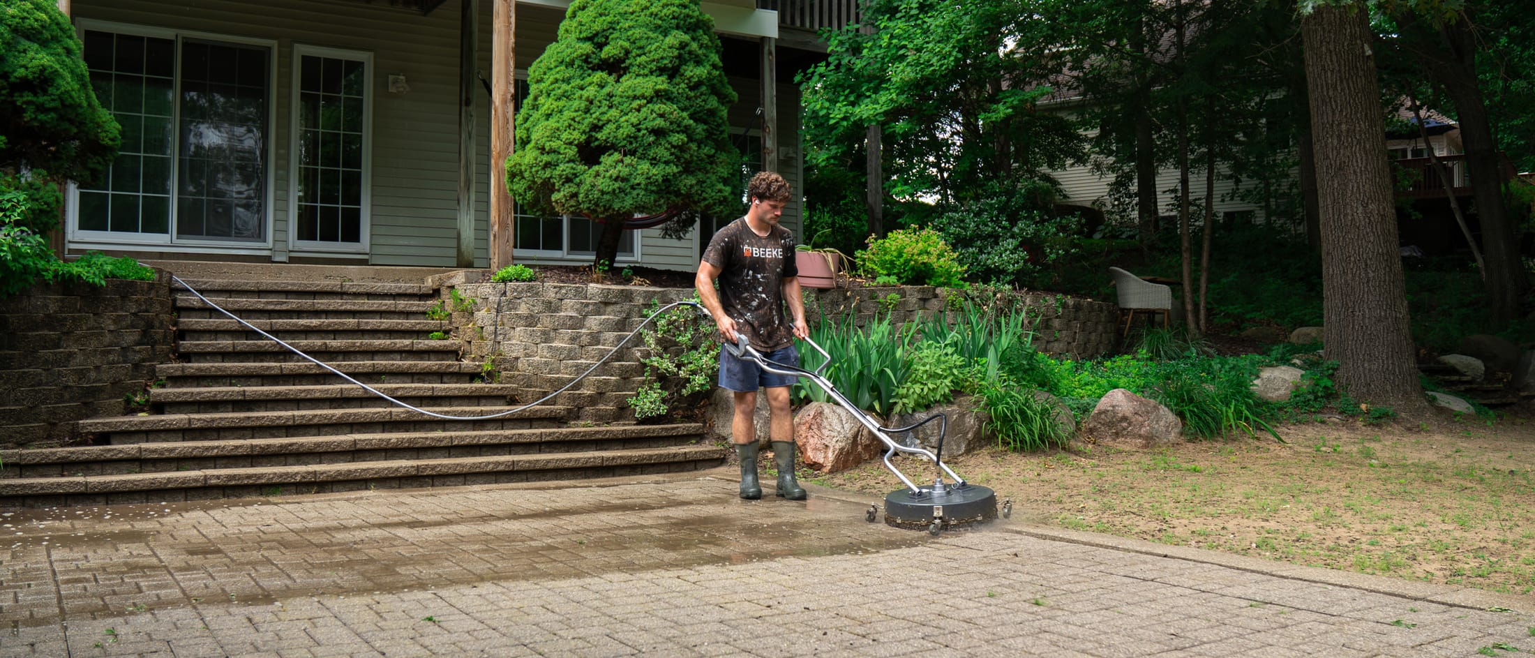 Rotary surface cleaner part-way across a brick paver patio, the cleaned pass visibly lighter than the untouched pavers beside it