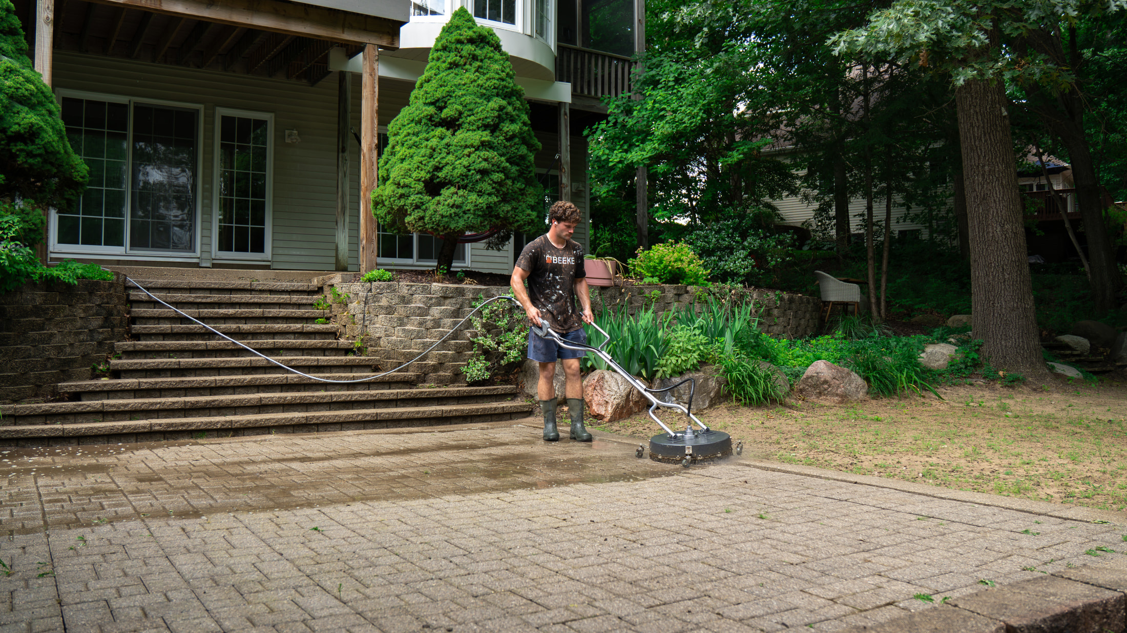 Rotary surface cleaner part-way across a paved surface — the cleaned pass visibly lighter than the stone beside it, the same process used for property managers & cre in the Grand Rapids metro